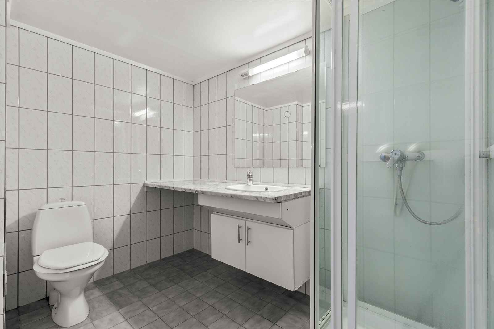 Badet er utstyrt med nedfelt servant, servantskap, WC og dusjkabinett. Det er også opplegg for vaskemaskin samt stikkontakt for tørketrommel, noe som gir en praktisk og arealeffektiv løsning i hverdagen. Galleribilde