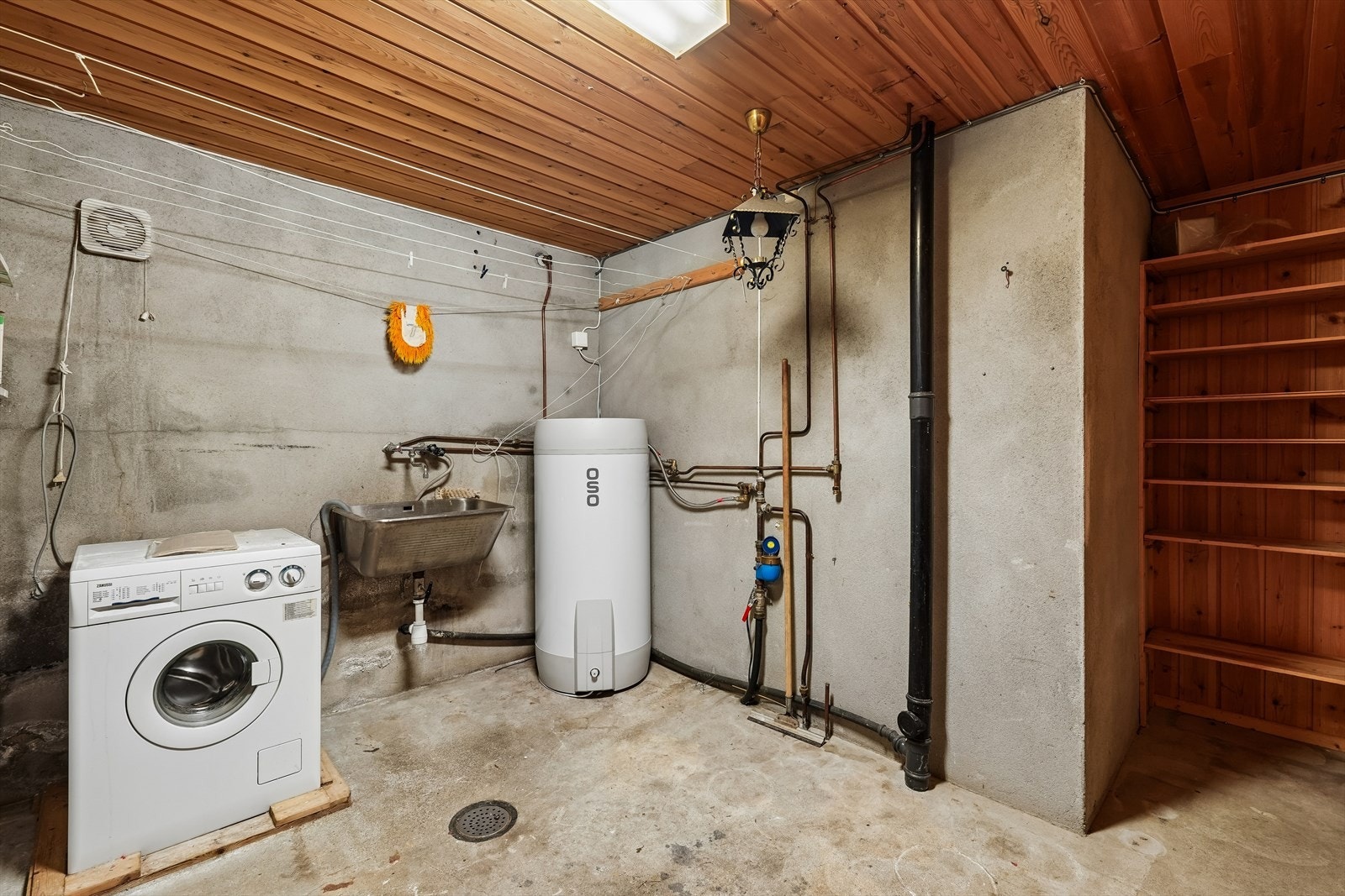 Videre finnes et praktisk vaskerom med vaskekum, opplegg for vaskemaskin og varmtvannsbereder. Rommet har sluk i gulvet, pussede vegger og betonggulv. Galleribilde