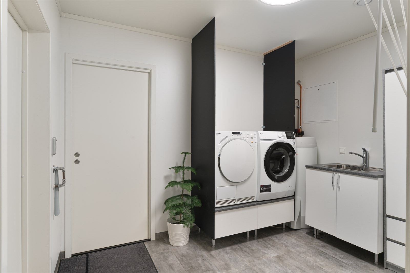 Praktisk vaskerom med flislagt gulv med gulvvarme, utslagsvask og opplegg for vaskemaskin. Galleribilde