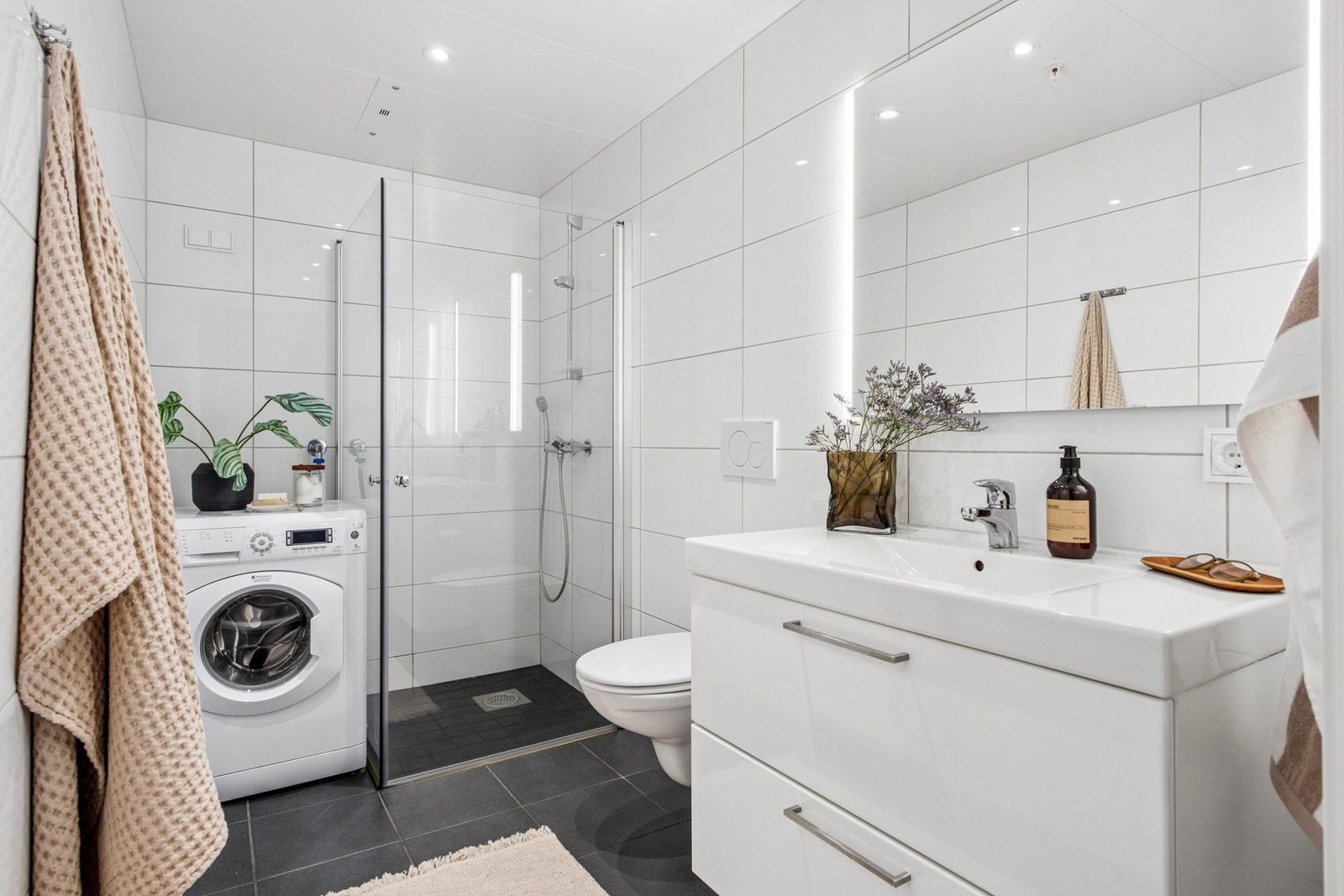 Badet er utstyrt med vegghengt toalett, dusjhjørne med glassdører og opplegg for vaskemaskin. Galleribilde