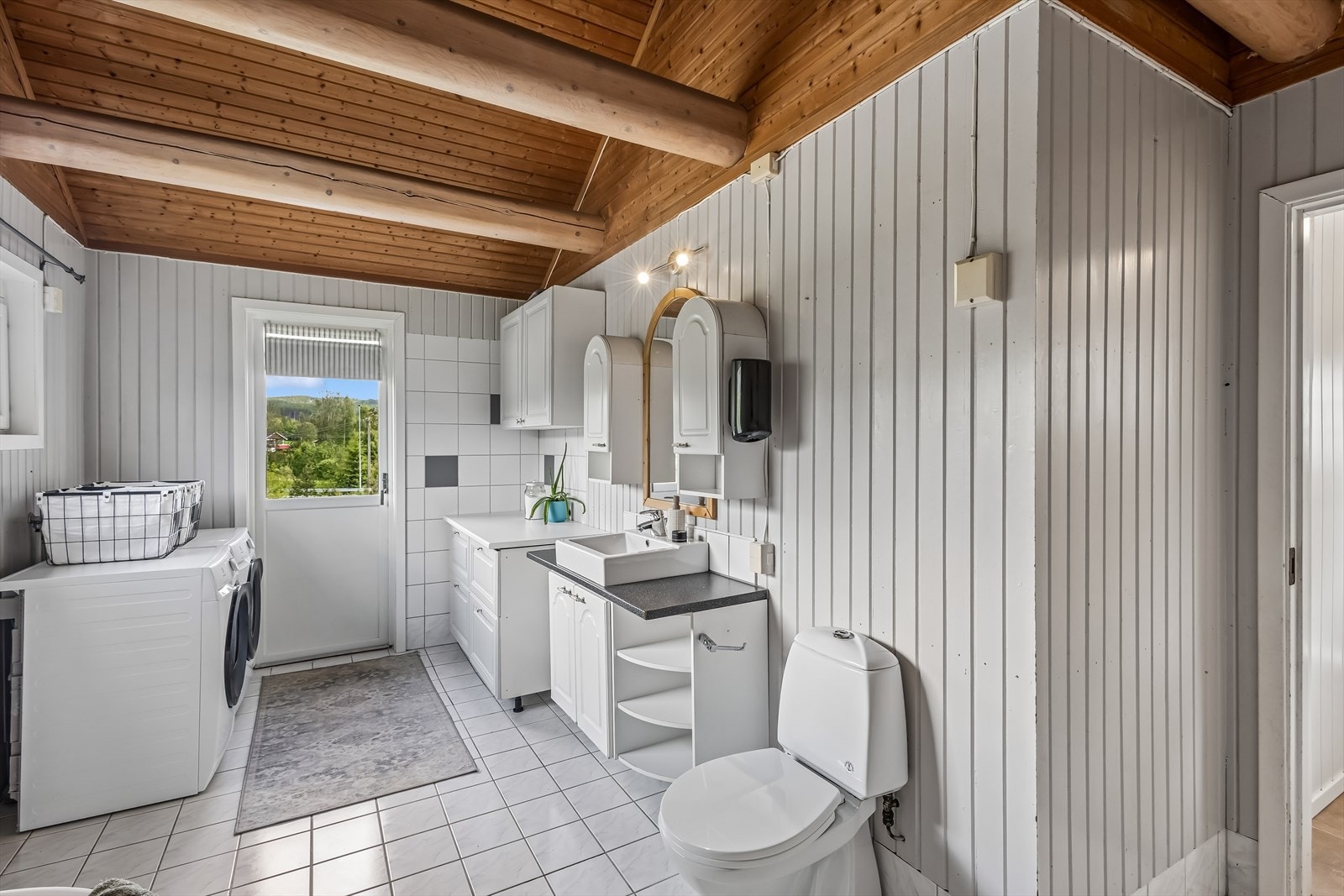 Rommet har fliser på gulv, malt trepanel på veggene og egen utgang til en platting. Galleribilde