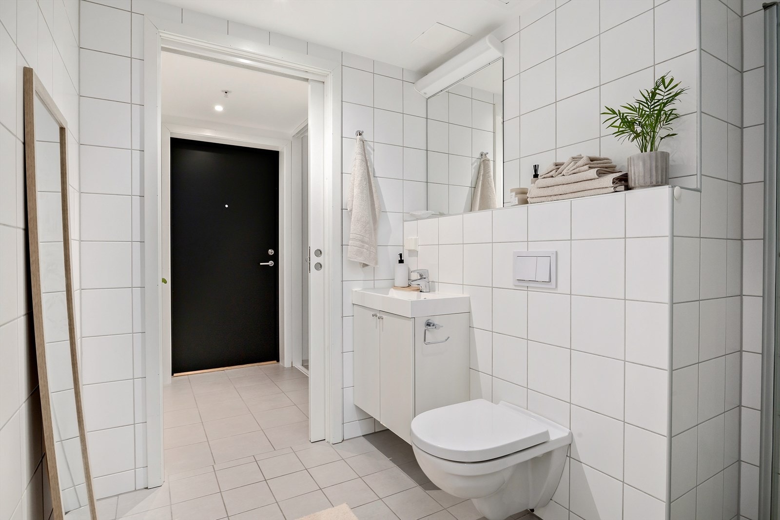 Badet er innredet med servantinnredning, speil og lys, vegghengt klosett og dusj på gulv med innfellbare glassdører. Galleribilde