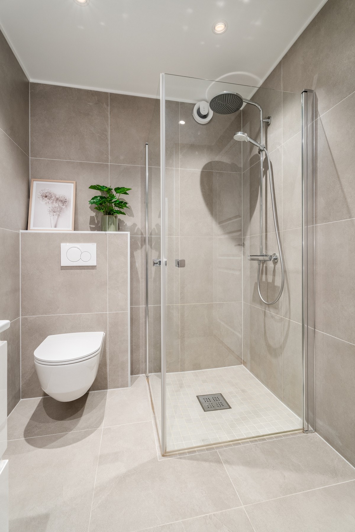 Badet har en delikat dusjsone med glassvegger og store 60 x 60 cm fliser på vegger og gulv, som bidrar til et moderne og stilrent uttrykk. Galleribilde
