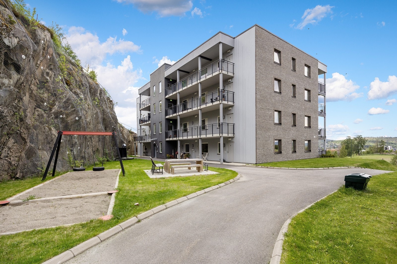 Det er pent opparbeidet rundt bygget med plen, asfalterte veier og planter i skråning. Bak bygget er uterommet godt skjermet av fjell, og her er det et huskestativ til de minste. Galleribilde
