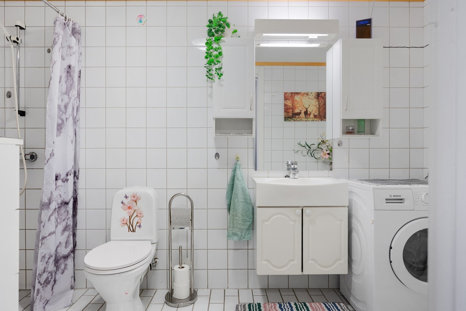 Badet er lyst med flislagte vegger og gulv med varmekabler. Hvit baderomsinnredning med heldekkende servant, speil og belysning. Toalett og dusjnisje med forheng. Galleribilde
