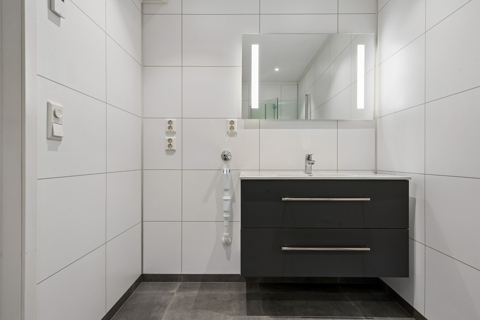 Badet er utstyrt med innredning med heldekkende servant, speil med integrert belysning og downlights i taket. Galleribilde