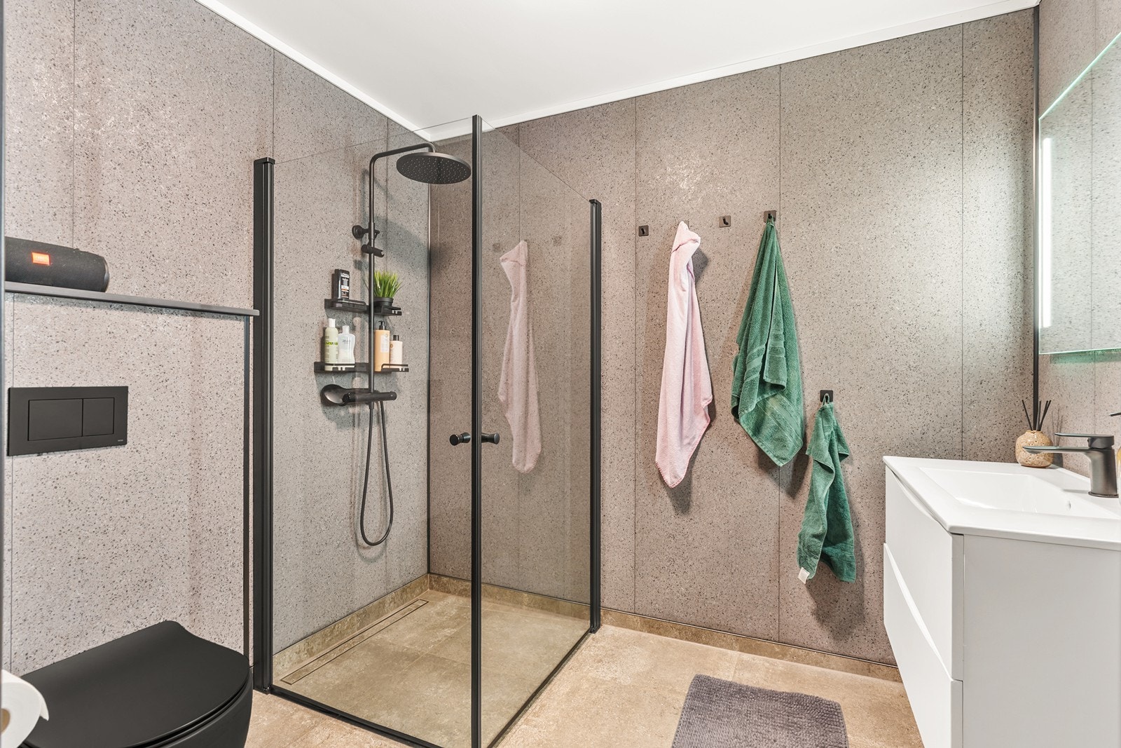 Badet er pent og moderne innredet med vegghengt toalett, baderomsinnredning og speil med integrert belysning. Dusjsonen har glassvegger og er utstyrt med "regndusj". Galleribilde