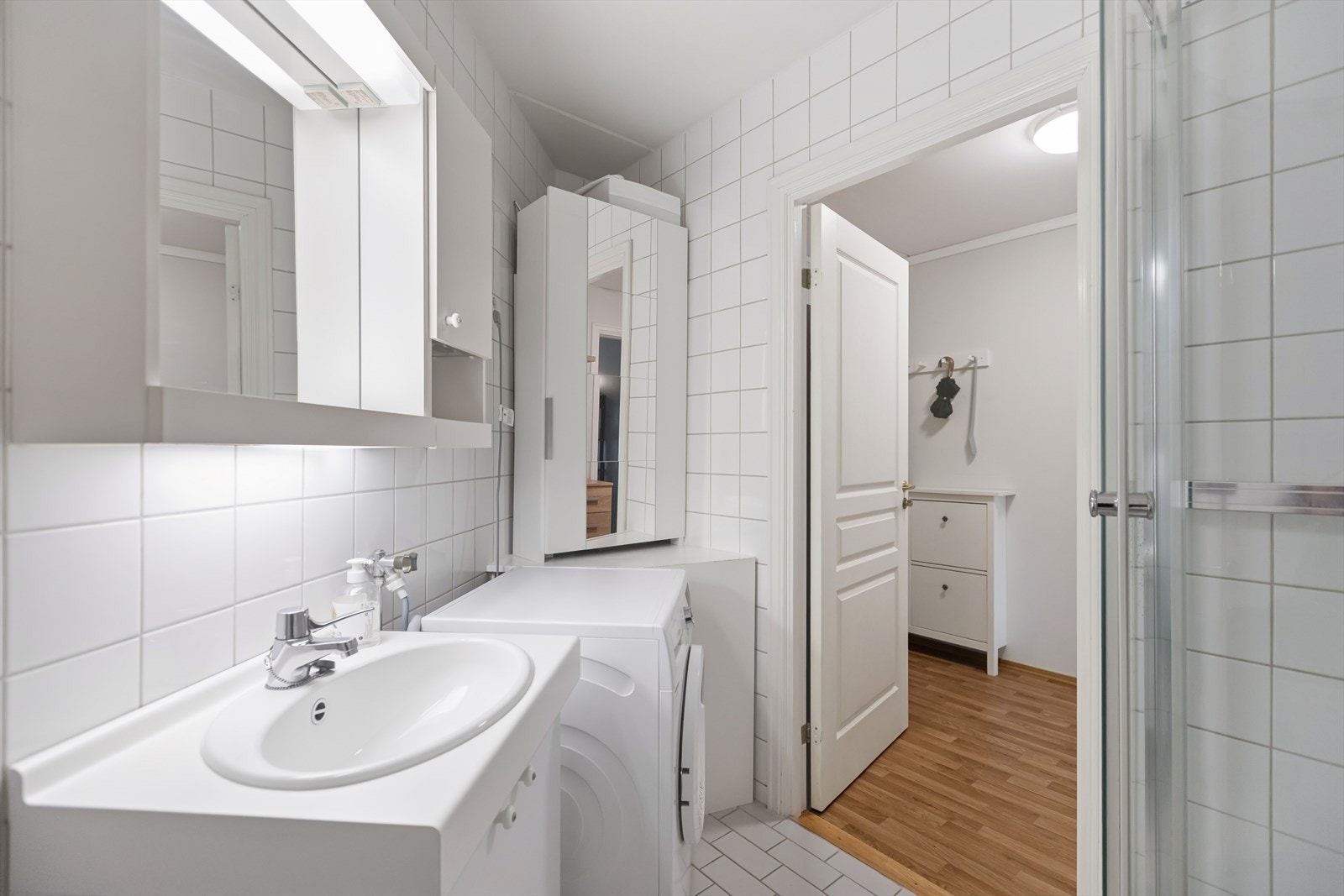 Flislagt bad med en praktisk planløsning bestående av dusjkabinett, servant med oppbevaring og toalett, samt opplegg for vaskemaskin. Galleribilde