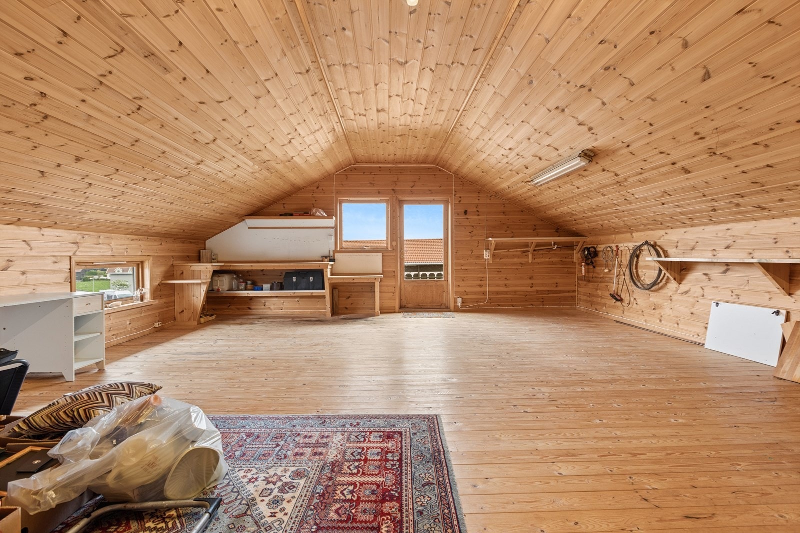 Et romslig loftsrom over garasjen med tregulv og panel i himlingen. Rommet har et stort potensial og kan benyttes til en rekke formål, enten det er lagring, hobbyrom eller annen fleksibel bruk. Galleribilde