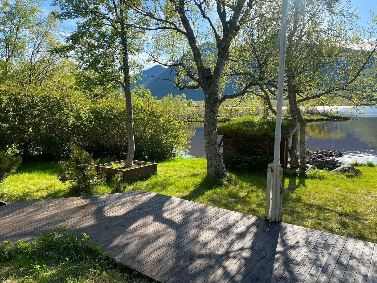 Utsikt fra platt mellom hytte og bod/parkering. Grillplass kan sees nederst mot vannet. Galleribilde