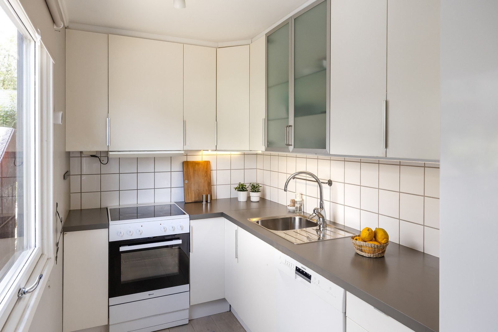 Lyst kjøkken vendt mot morgensola som kommer inn i en åpen passasje mellom naborekkene på baksiden av huset. Galleribilde