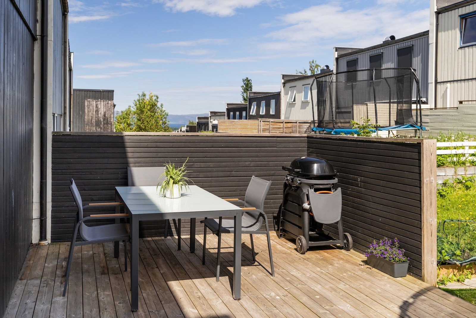 Lun terrasse på baksiden av huset med levegger og god plass til romslige sittegrupper, samt romslig hagefelt med god boltreplass. Galleribilde