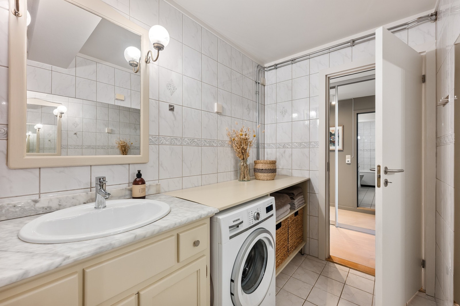 Badet er flislagt og har en praktisk innredning med servantinnredning, speil med belysning, toalett, badekar og opplegg for vaskemaskin. Galleribilde