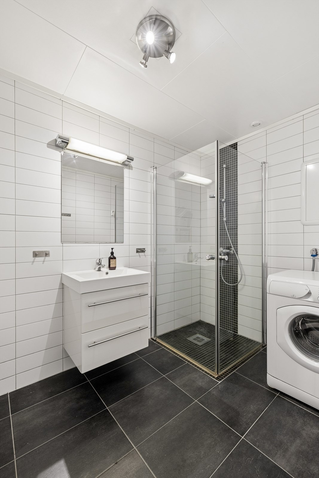 Badet er utstyrt med dusjvegger, gulvmontert toalett og servant med underskap. Galleribilde