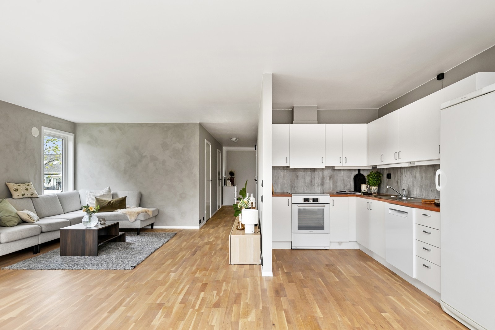 Tidløst kjøkken i hvit utførelse med slette fronter og plate over benk som står i stil med boligens øvrige fargevalg. Galleribilde