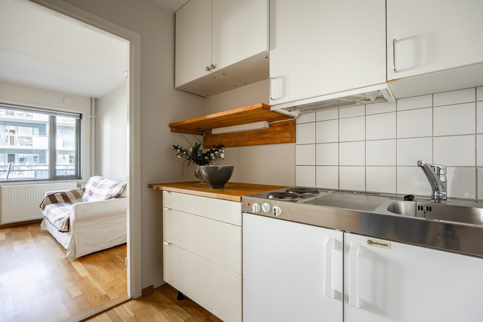 Hybelkjøkken med glatte fronter, benkeplate i tre og benkebeslag med nedfelt oppvaskkum og platetopp. Galleribilde