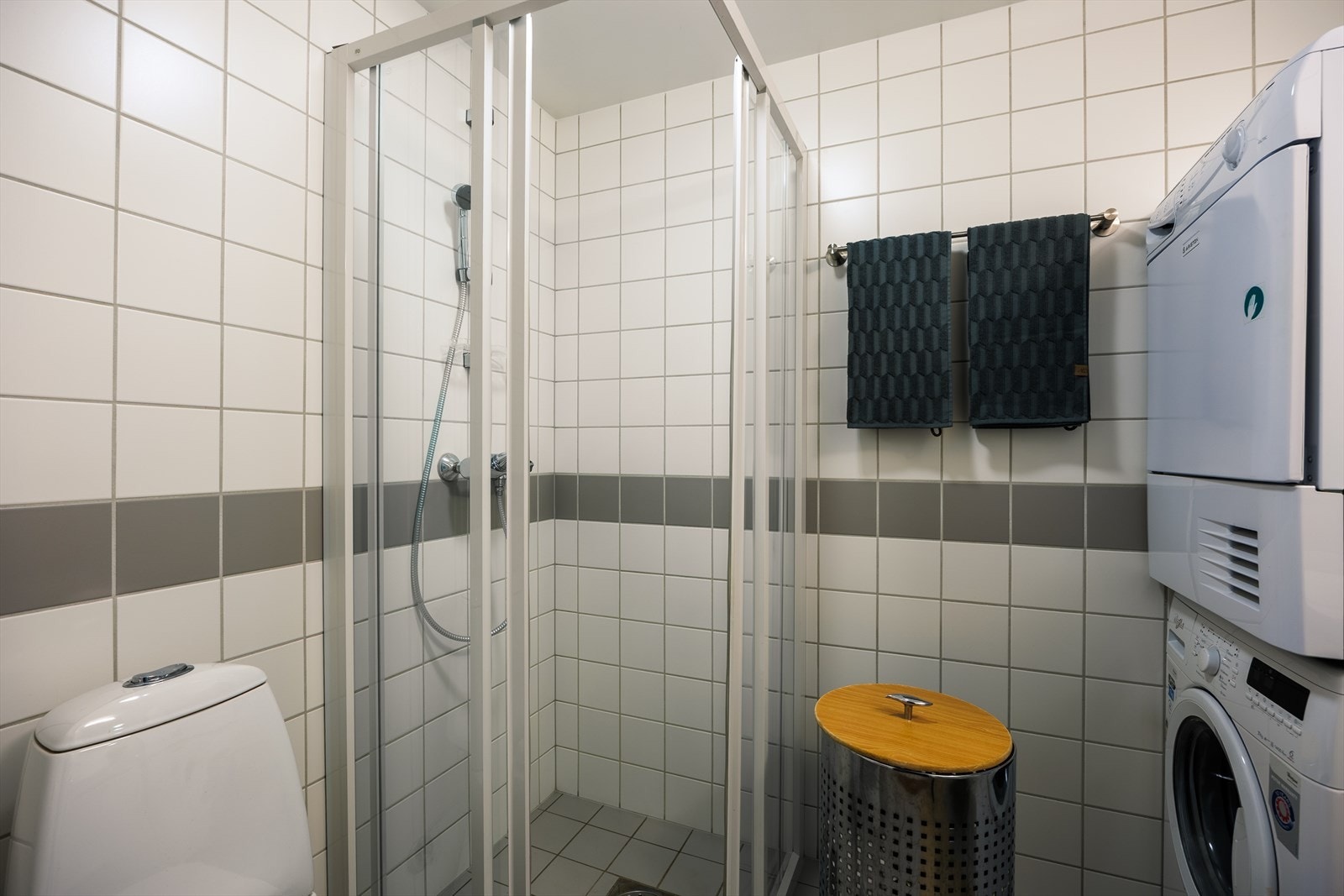 Badet er fra 2005. Baderommet har lysegrå fliser på gulv med gulvvarme, hvite fliser på vegger og avtrekksventil i himling. Avtrekket styres fra kjøkkenviften. Galleribilde