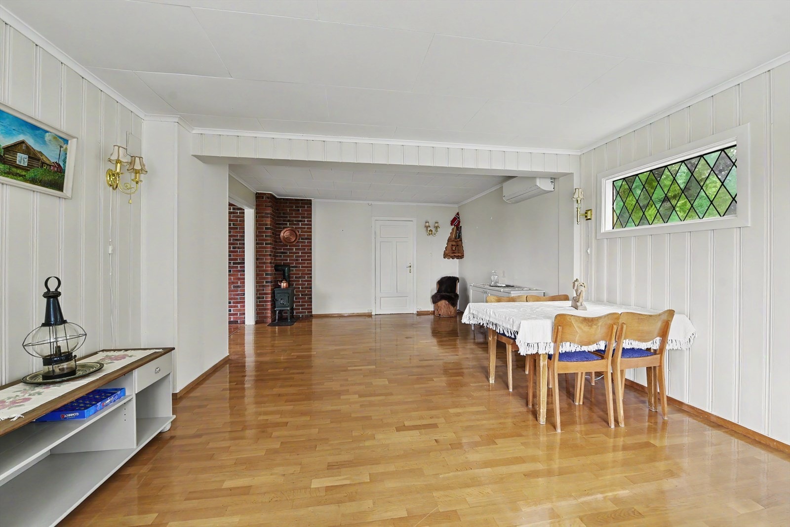 Stuen er en del av et tilbygg fra 1972 og har overflater med malt panel og parkett. Galleribilde