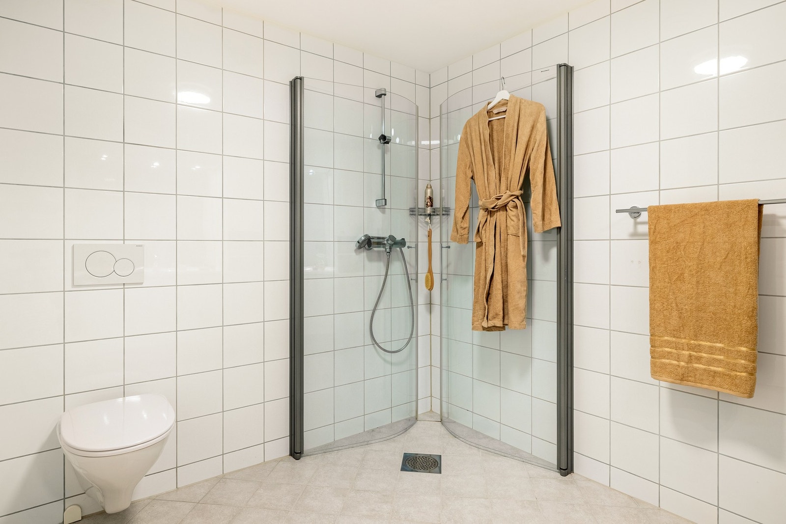 Badet er innredet med vegghengt toalett, servant med innredning, høyskap og dusjhjørne. Galleribilde