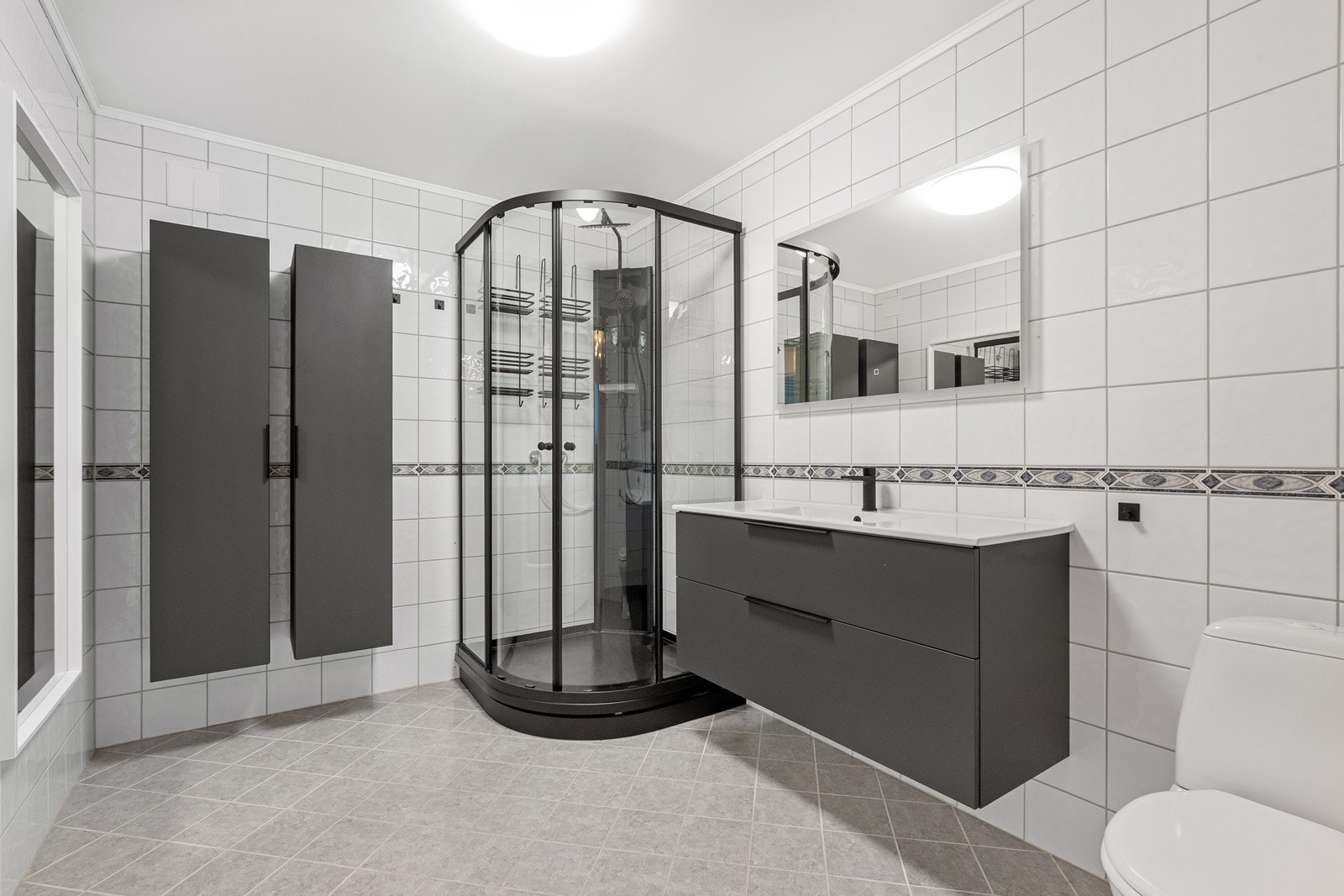 Badet, med flislagte vegger og gulv, er utstyrt med dusjkabinett og elektriske varmekabler. Galleribilde