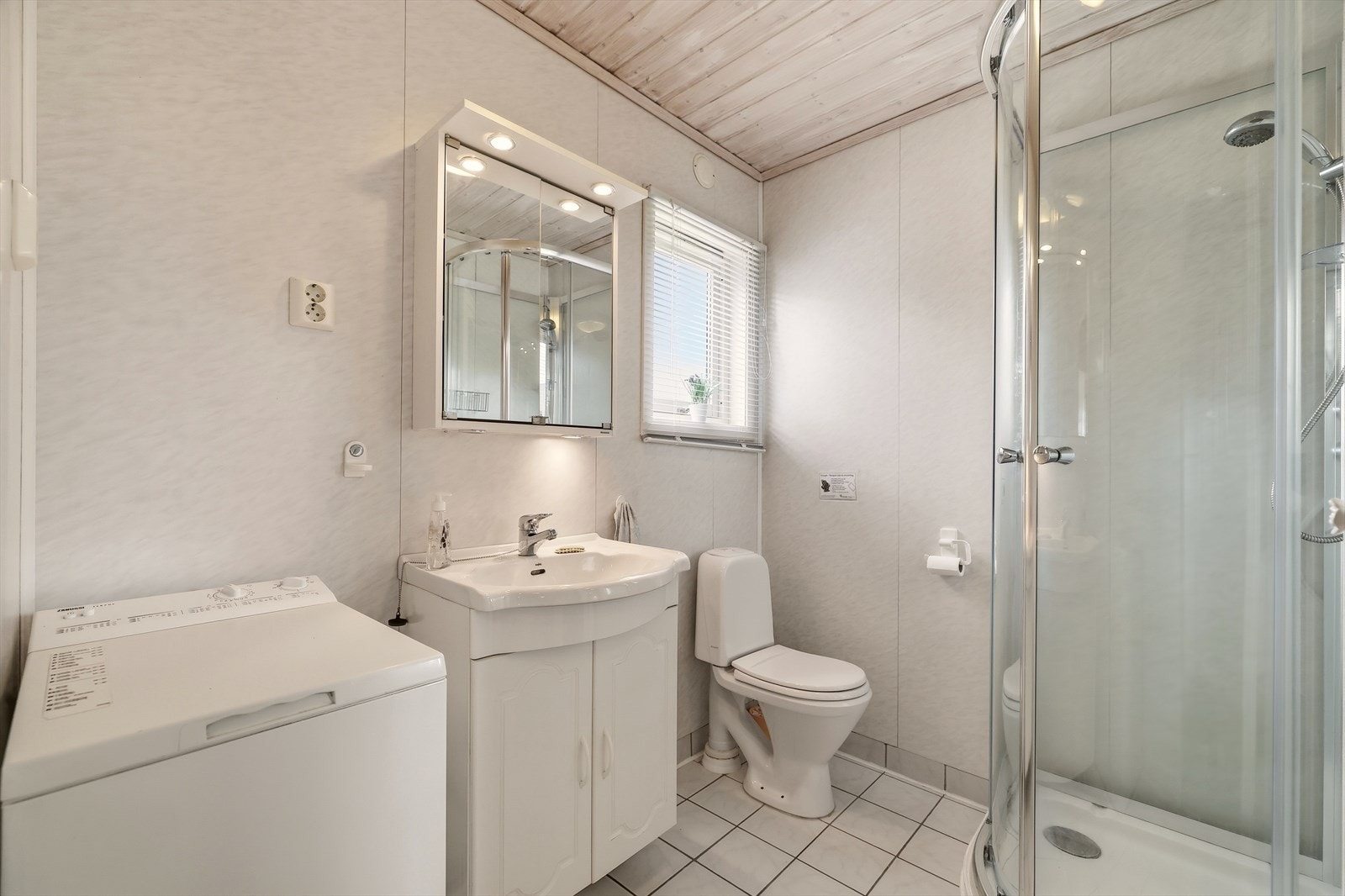 Badet er praktisk innredet med baderomsmøbel med servant, speilskap med belysning, dusjkabinett, gulvstående toalett og opplegg for vaskemaskin. Galleribilde