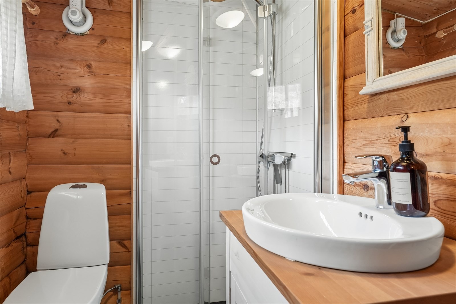 Badet er utstyrt med toalett, servantskap med porselensservant og ettgreps armatur, samt dusjnisje med baderomsplater og praktiske dusjvegger i glass som kan foldes inn når de ikke er i bruk. Galleribilde