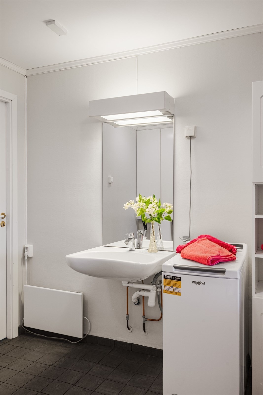 Veggmontert servant med speil og lys med elektrisk uttak i overkant. Det er opplegg for vaskemaskin på badet. Galleribilde