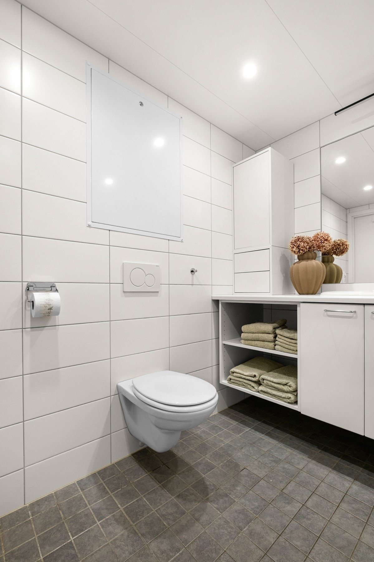 Badet er innredet med servantinnredning, veggmontert toalett, dusjhjørne med innfellbare glassdører og opplegg til vaskemaskin Galleribilde