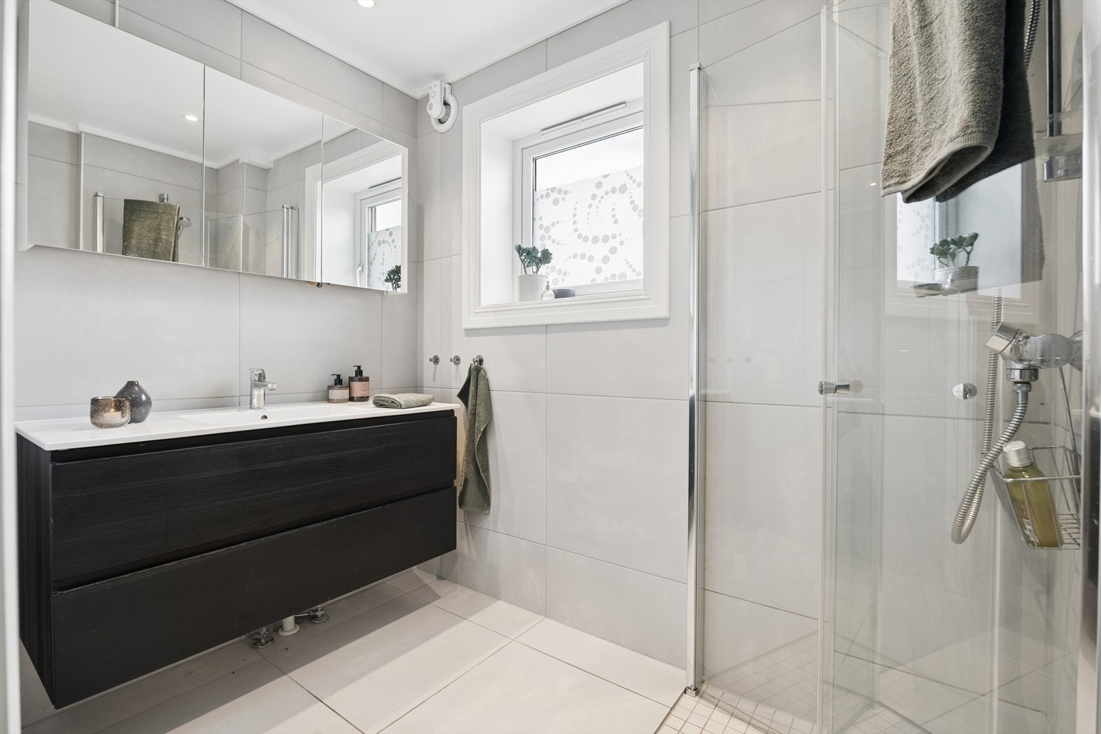 Badet er moderne og helfliset, utstyrt med baderomsinnredning med nedfelt servant. Dusjen har glassvegger og garnityr på vegg. Galleribilde