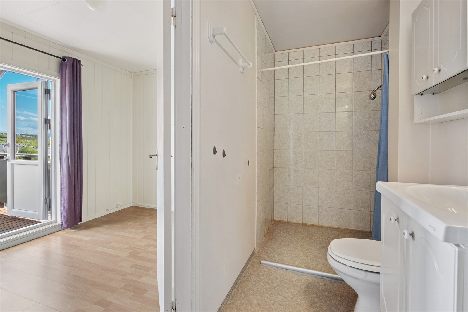 Badet er av eldre dato og er innredet med en kombinasjon av grått vinylbelegg på gulv og en kombinasjon av sjatterte fliser og malte flater på vegg. Galleribilde