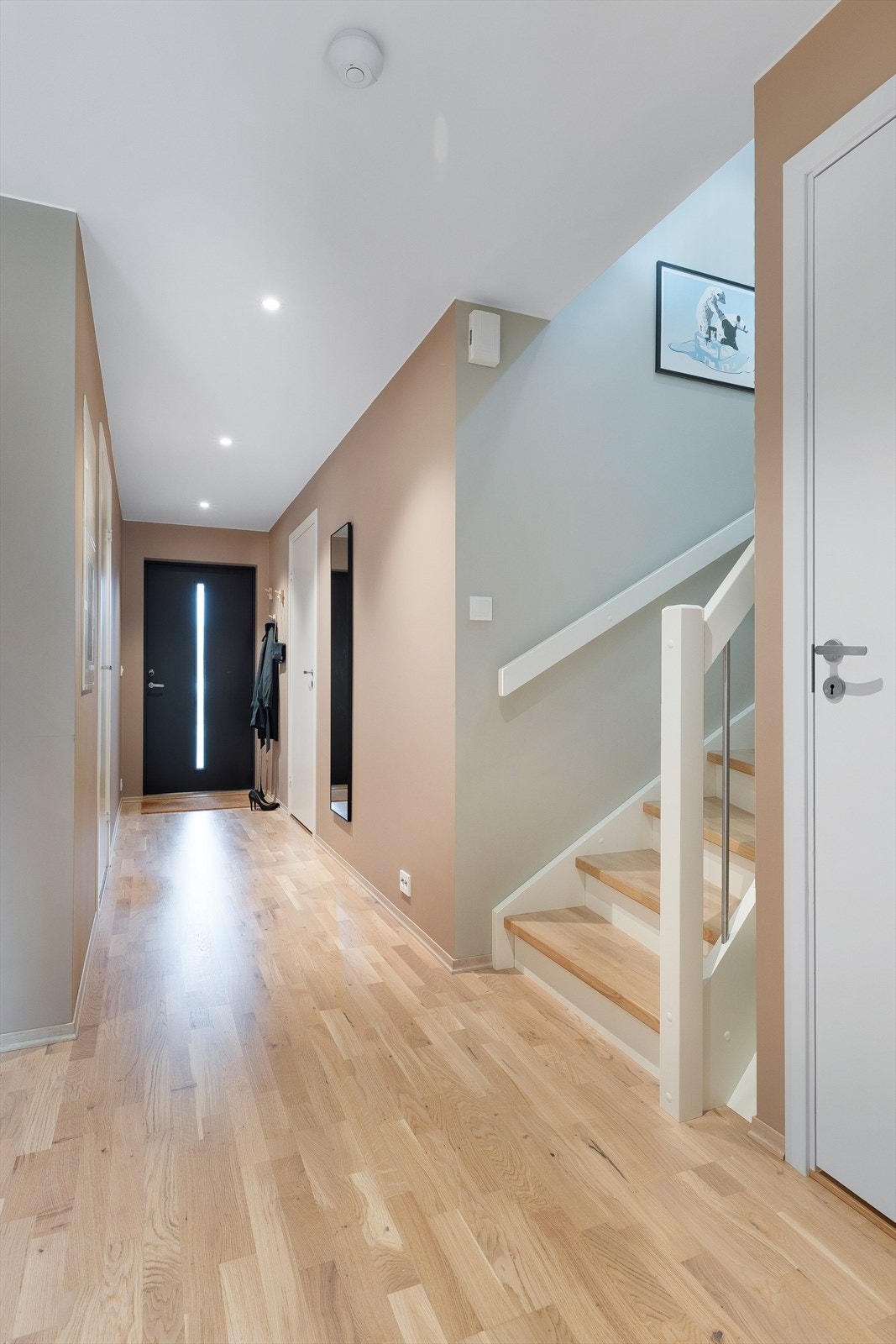 Romslig entré med parkett på gulv. Den lakkerte tretrappen leder opp til boligens sosiale sone i andre etasje. Galleribilde