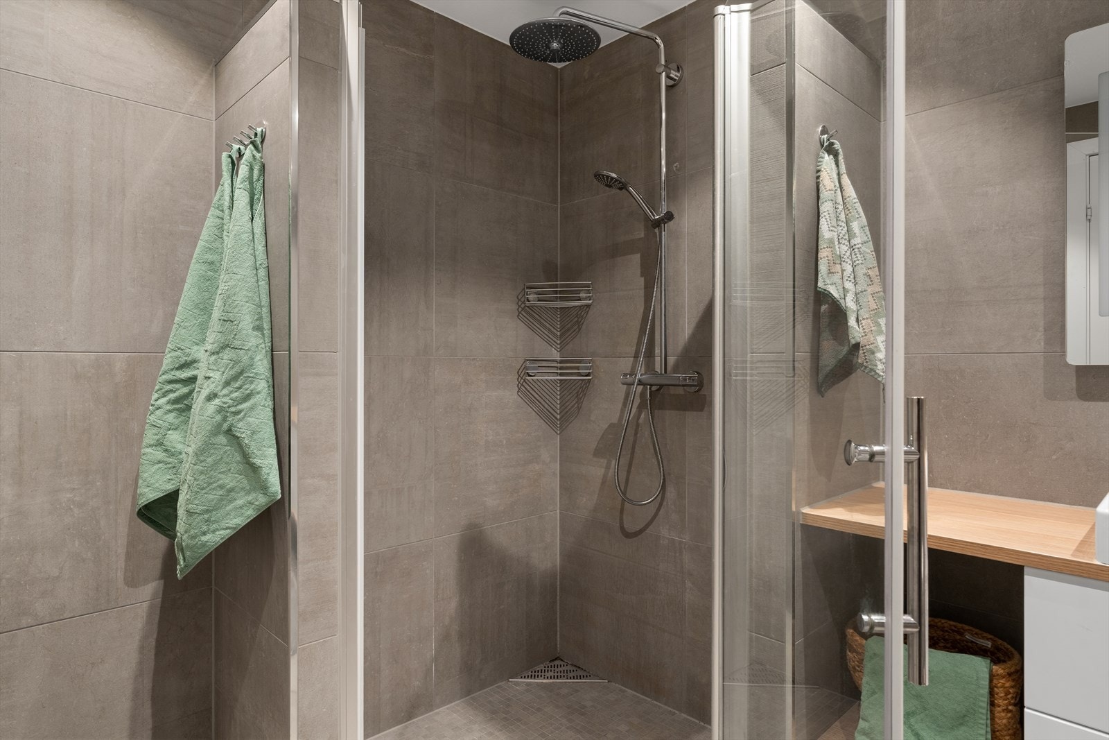 Badet er utstyrt med dusjhjørne med glassdør og hjørnesluk i dusjsonen, vegghengt toalett med innebygd sisterne samt baderomsinnredning med servant og speil med integrert belysning Galleribilde
