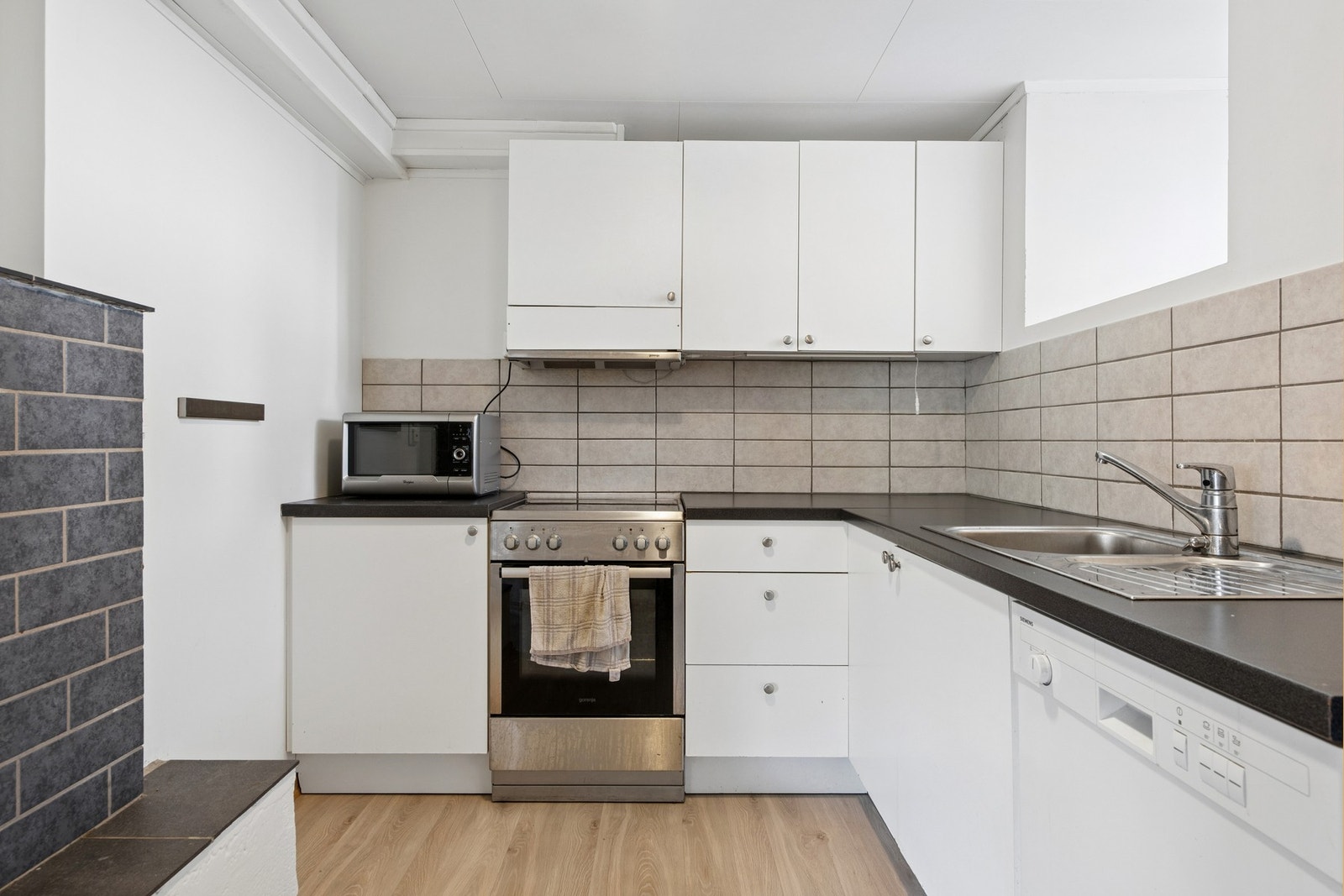 Kjøkken i hybelleiligheten, utstyrt med frittstående hvitevarer og kjøkkenventilator med avtrekk ut. Galleribilde