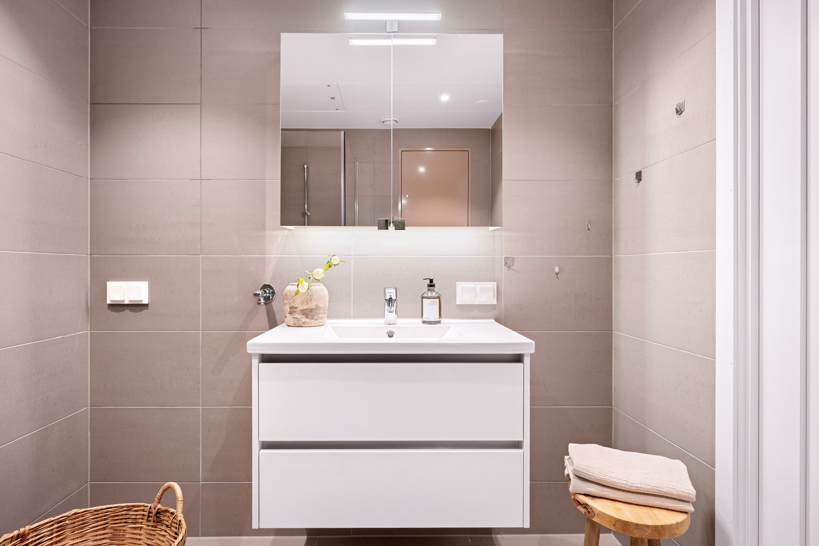 Badet er innredet med vegghengt servantinnredning, speilskap med belysning, vegghengt toalett og dusjhjørne med glassvegg. Galleribilde