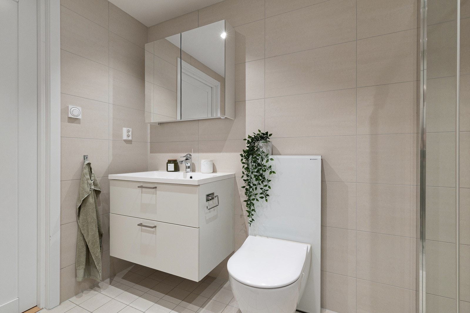 Innredning og garnityr på badet består av veggmontert toalett (GEBERIT), dusjplass med inn-utadslående dusjvegger og bredt baderomsmøbel med servant med ettgreps blandebatteri og speilskap. Galleribilde