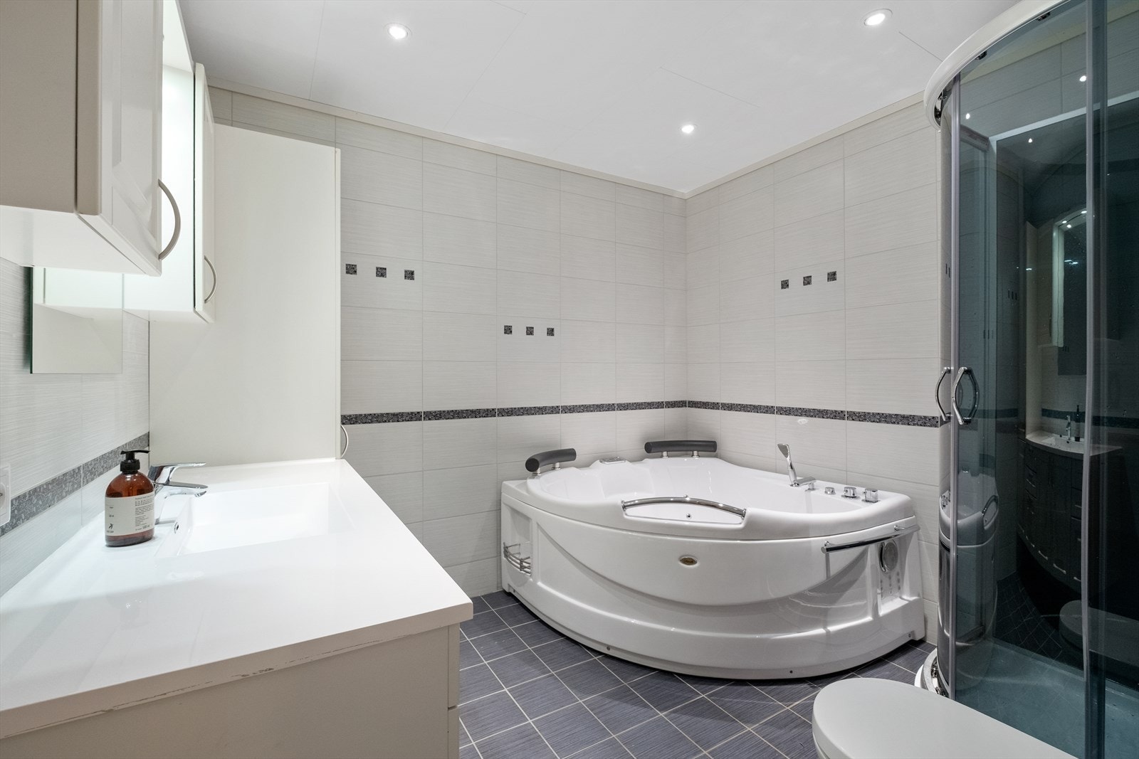 Badet har innredning med heldekkende servant, overskap, høyskap speil med lys, veggmontert toalett, dusjkabinett og badekar. Galleribilde