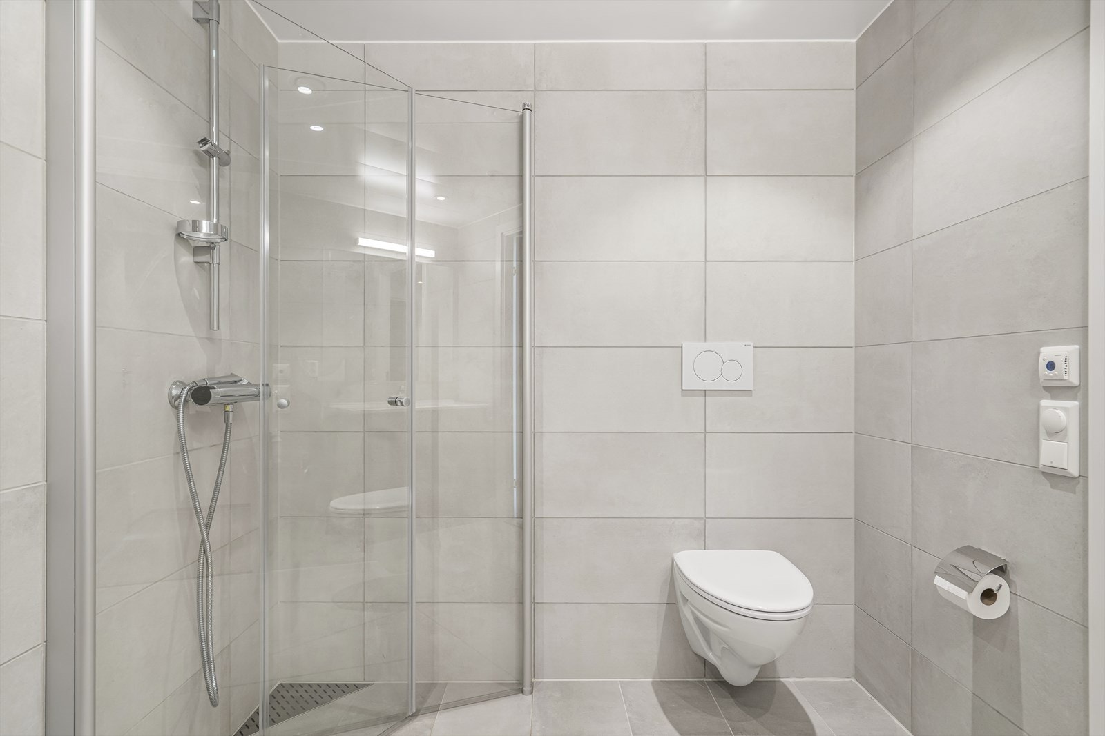Badet er utstyrt med vegghengt toalett, dusjhjørne m/innfellbare glassdører og baderomsinnredning. Galleribilde