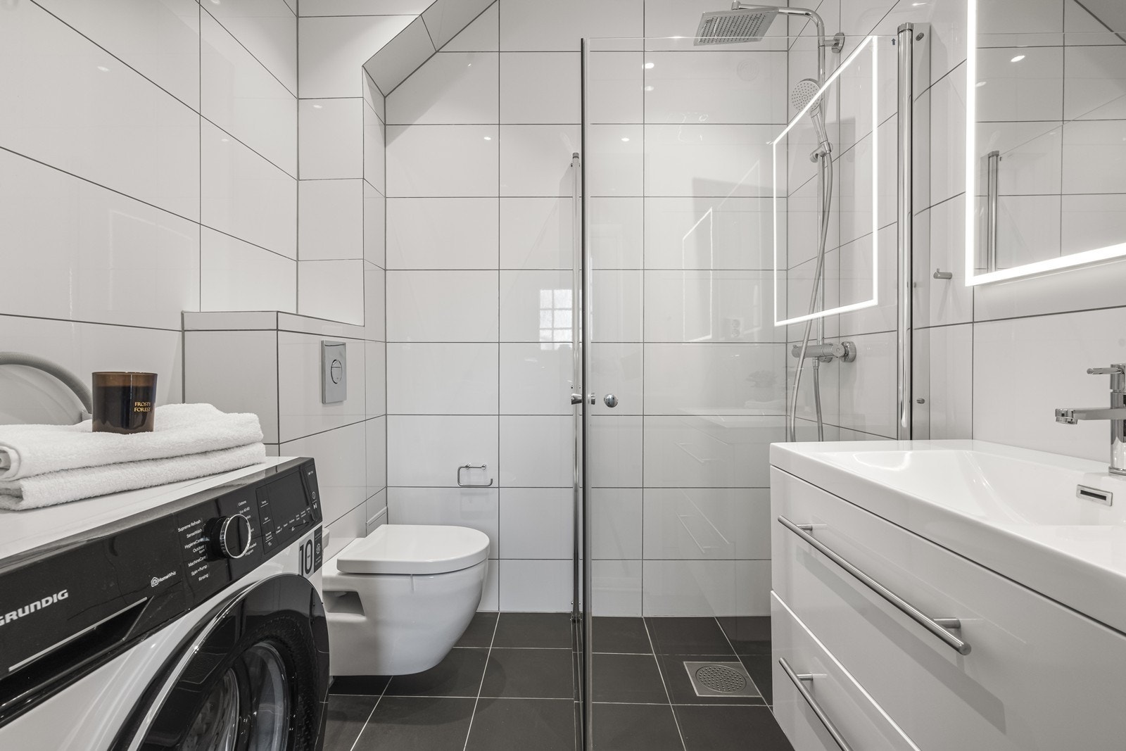 Badet har flislagte overflater, gulvvarme og rikelig med lys i downlights og speil. Speilet var nytt i 2025. Galleribilde