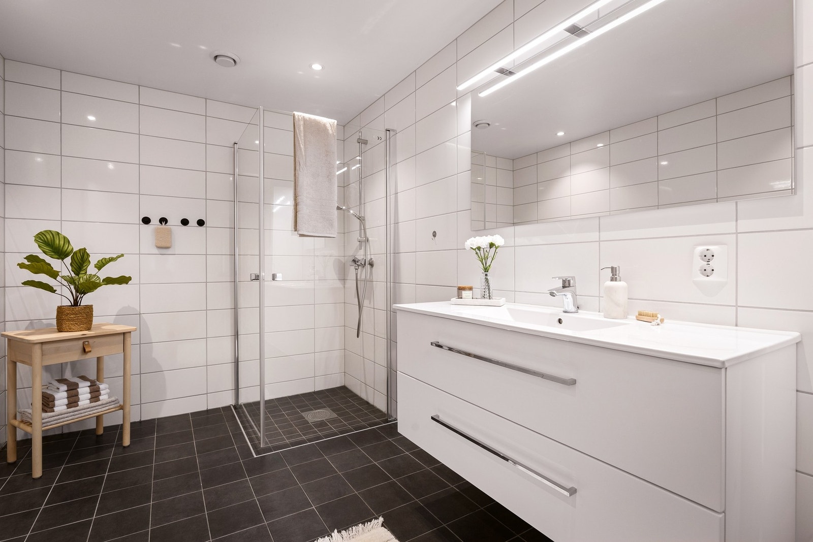 Rommet er innredet med flislagte gulv- og veggoverflater, malt tak med innfelte downlights, vegghengt toalett, servantinnredning med skuffer og speil med belysning. Galleribilde
