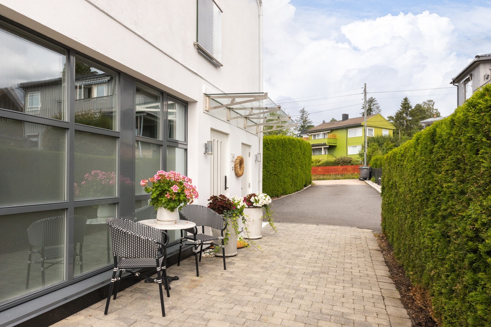 Ved inngangen er det asfaltert adkomst, steinbelagt uteområde, glassoverbygg og moderne utebelysning. Galleribilde