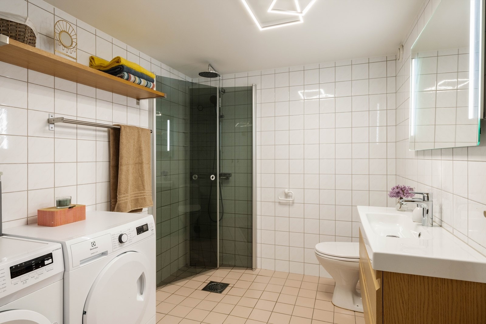 Romslig baderom med dusjhjørne med svingdør, servantskap i glatt utførelse med heldekkende servant, speil med integrert LED-lys og WC. Galleribilde
