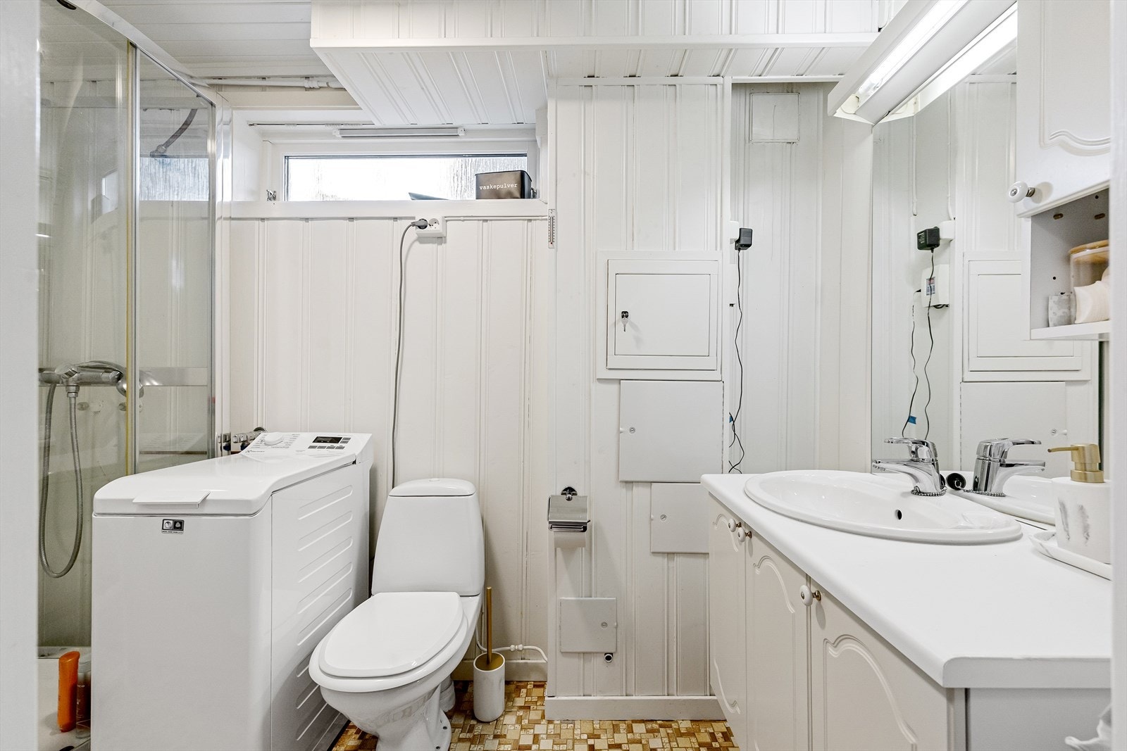 Badet er av eldre dato og er innredet med dusjkabinett, gulvstående toalett, servantinnredning, speil og opplegg for vaskemaskin. Galleribilde