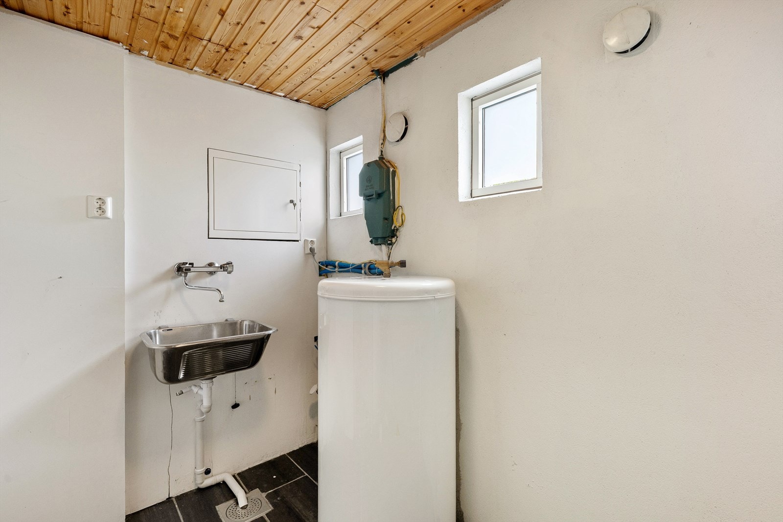 Praktisk vaskerom med flislagt gulv, opplegg for vaskemaskin og vaskekar i stål. Galleribilde
