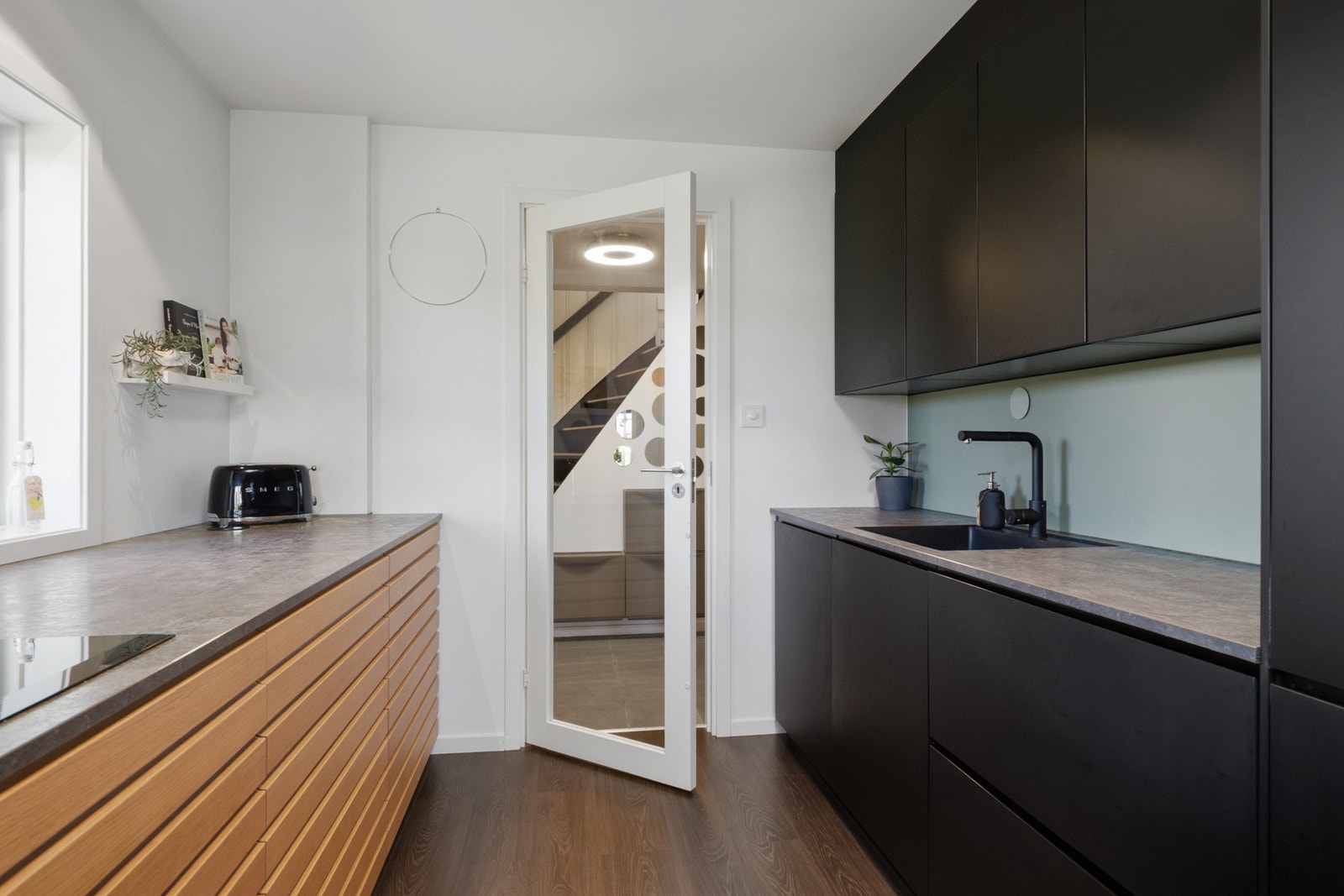 Innredningen har takhøye skap med sorte, matte fronter, kombinert med trehvite lamellfronter på benken og benkeplate i tynn, grå laminat. Galleribilde