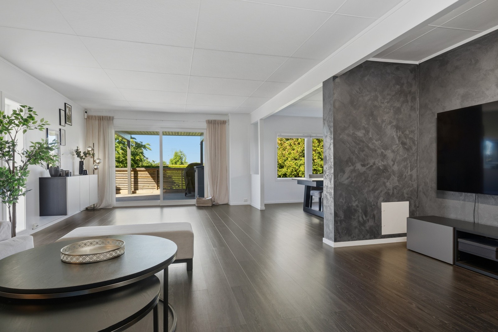 Stuen har enstavs laminatgulv i mørkt design, glatte, lysmalte veggflater og hvitmalt himling med listdekor. Galleribilde