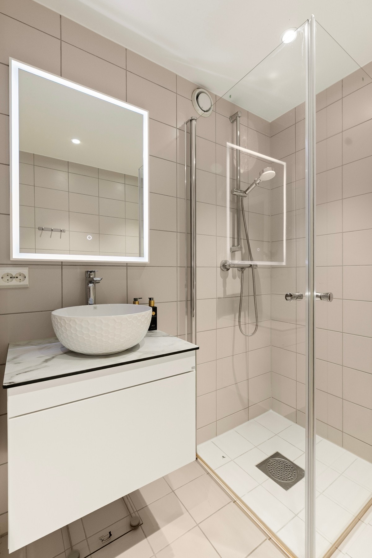 Badet er innredet med moderne baderomsinnredning med servant og speil, samt en romslig dusjnisje med glassdører. Galleribilde