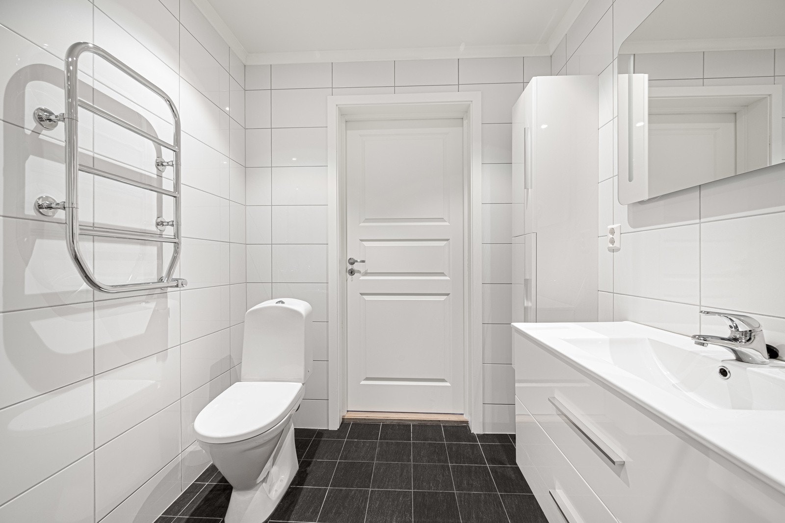 Badet har dusjhjørne, servant i innredning med skuffer, speil, høyskap, toalett og opplegg for vaskemaskin Galleribilde