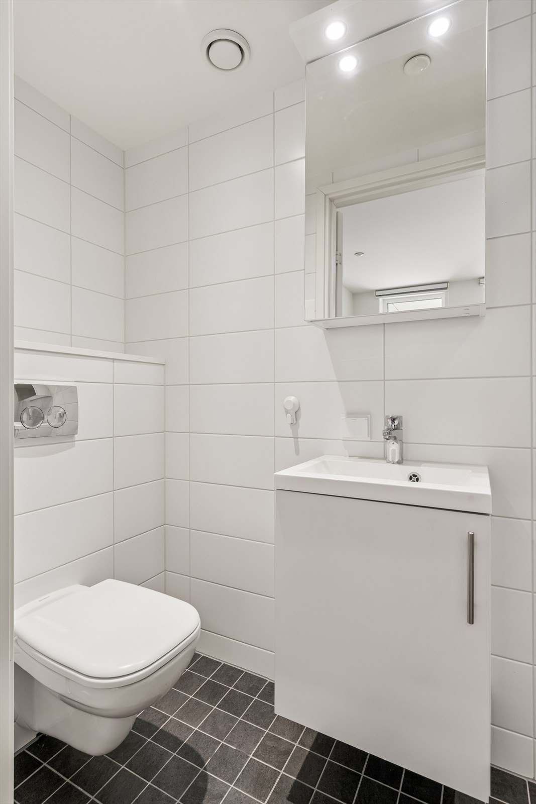 Badet er utstyrt med veggmontert toalett, servant i innredning og speilskap med lys. Galleribilde