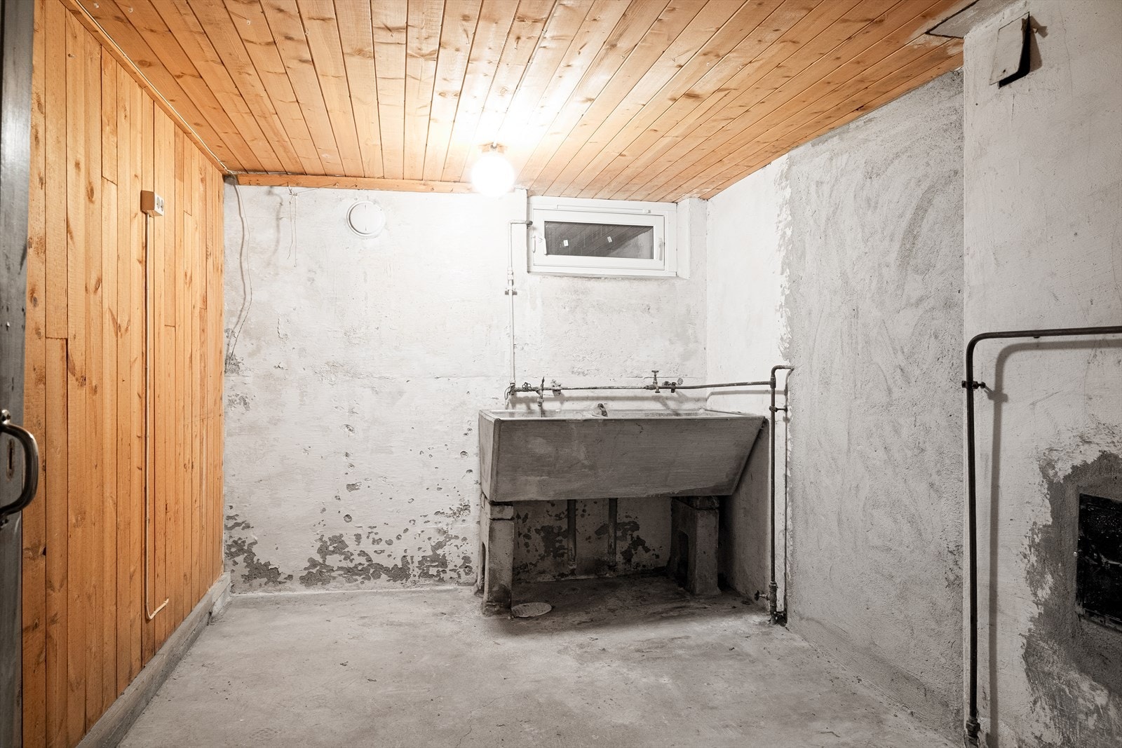 Kjellerens vaskerom med en betongvask og varmtvannsbereder. Galleribilde