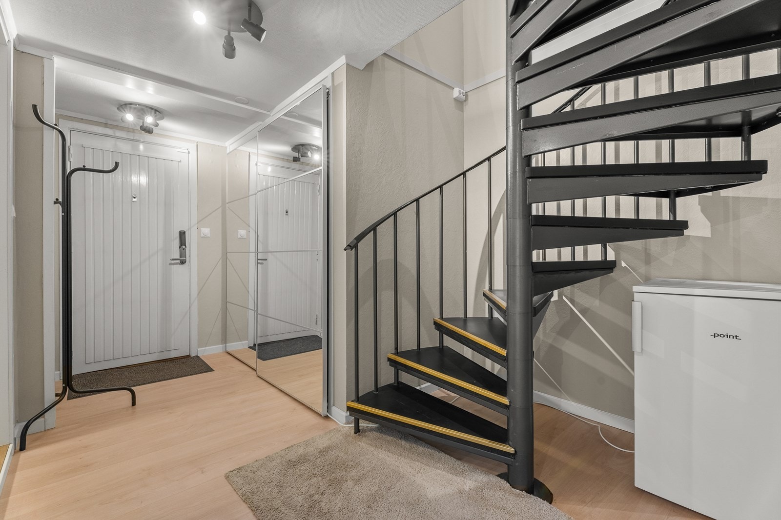 Gangen har plass til oppbevaring i skyvedørsgarderobe og en spiraltrapp som forbinder leilighetens to etasjer - Her ønskes du velkommen inn! Galleribilde